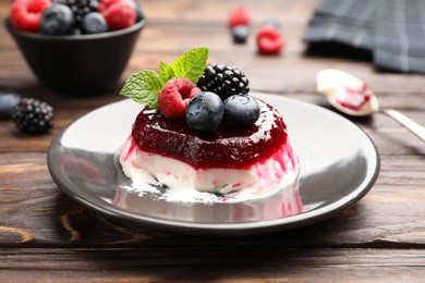 Photo of Delicious panna cotta with berries, jam and mint on wooden table, closeup