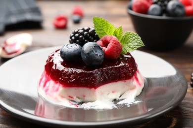 Photo of Delicious panna cotta with berries, jam and mint on wooden table, closeup