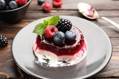 Photo of Delicious panna cotta with berries, jam and mint on wooden table, closeup