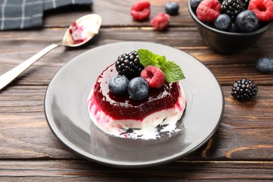 Photo of Delicious panna cotta with berries, jam and mint on wooden table, closeup