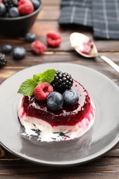 Photo of Delicious panna cotta with berries, jam and mint on wooden table, closeup