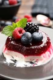 Photo of Delicious panna cotta with berries, jam and mint on table, closeup
