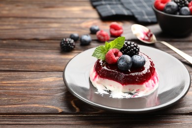Photo of Delicious panna cotta with berries, jam and mint on wooden table, closeup