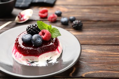 Photo of Delicious panna cotta with berries, jam and mint on wooden table, closeup