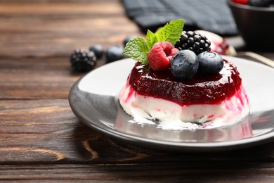 Photo of Delicious panna cotta with berries, jam and mint on wooden table, closeup