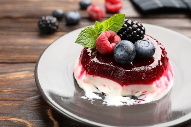 Photo of Delicious panna cotta with berries, jam and mint on wooden table, closeup
