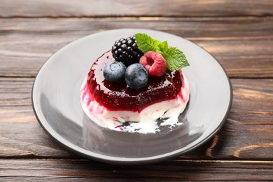 Photo of Delicious panna cotta with berries, jam and mint on wooden table, closeup