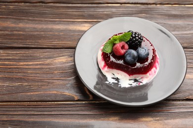 Photo of Delicious panna cotta with berries, jam and mint on wooden table, closeup. Space for text