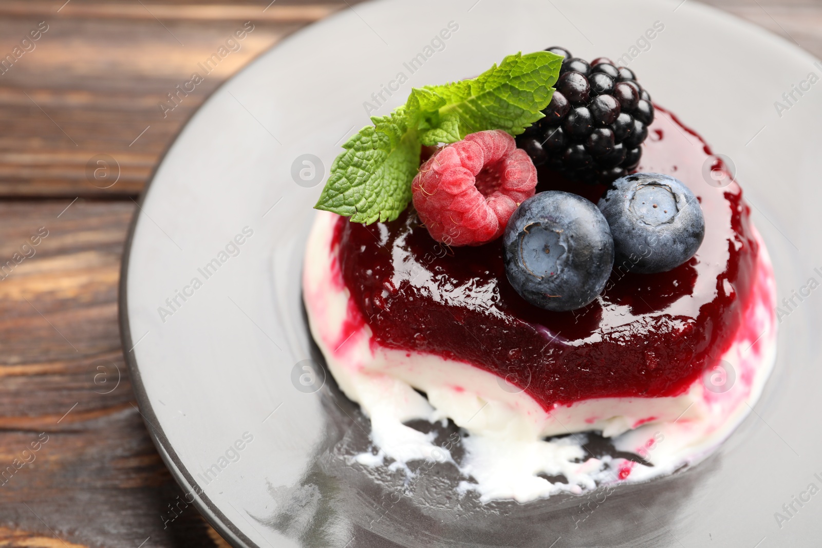 Delicious panna cotta with berries, jam and mint on wooden table, closeup Photo of Delicious panna cotta with berries, jam and mint on wooden table, closeup