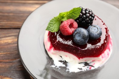 Photo of Delicious panna cotta with berries, jam and mint on wooden table, closeup