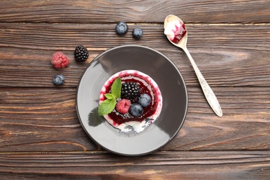 Photo of Delicious panna cotta with berries, jam and mint on wooden table, flat lay