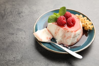 Photo of Delicious panna cotta with berries, sauce and mint on grey textured table, closeup. Space for text