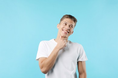 Photo of Dream come true. Positive young man wishing for something on light blue background
