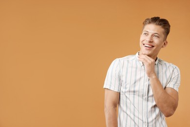 Photo of Dream come true. Positive young man thinking about something on brown background. Space for text