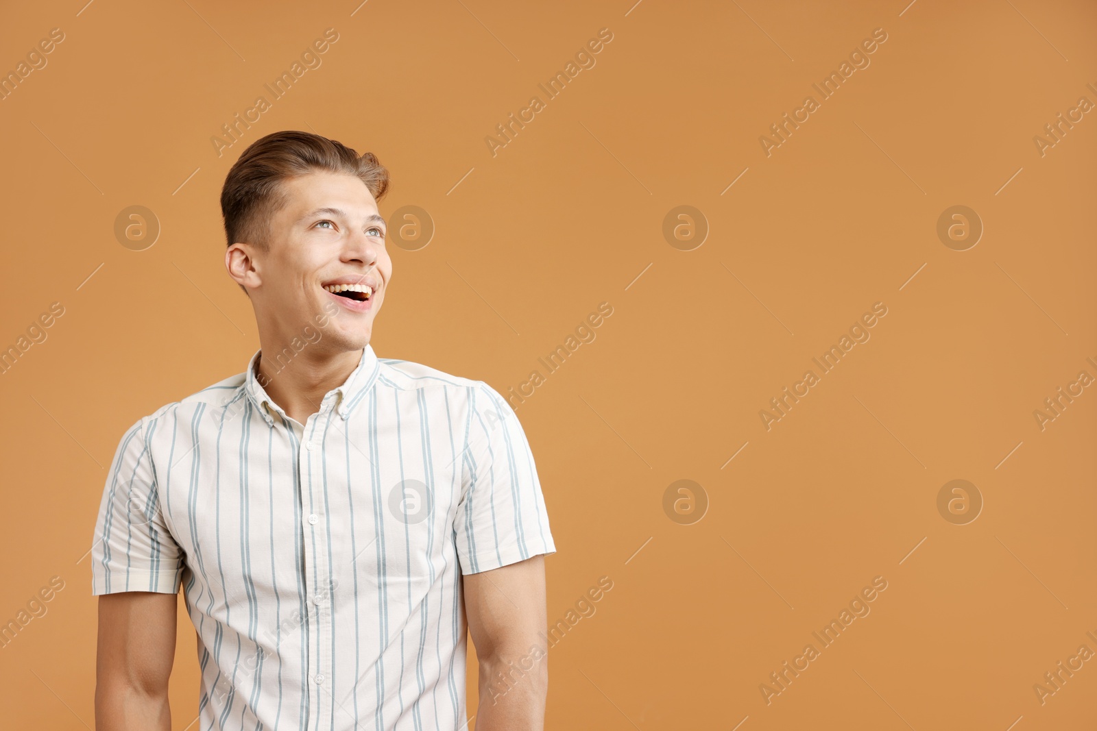 Photo of Dream come true. Positive young man thinking about something on brown background. Space for text