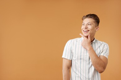 Photo of Dream come true. Positive young man thinking about something on brown background. Space for text