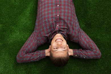 Photo of Dream come true. Positive young man thinking about something while lying on green grass, top view