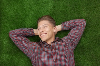 Photo of Dream come true. Positive young man thinking about something while lying on green grass, top view