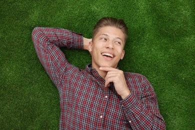 Photo of Dream come true. Positive young man thinking about something while lying on green grass, top view