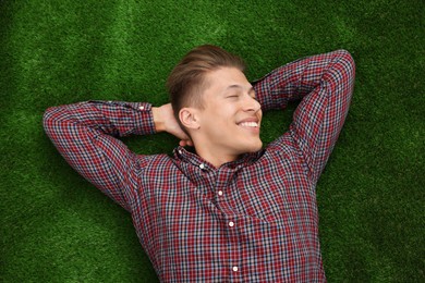 Photo of Dream come true. Positive young man thinking about something while lying on green grass, top view