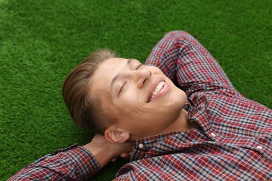 Photo of Dream come true. Positive young man thinking about something while lying on green grass