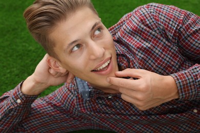 Photo of Dream come true. Positive young man thinking about something while lying on green grass