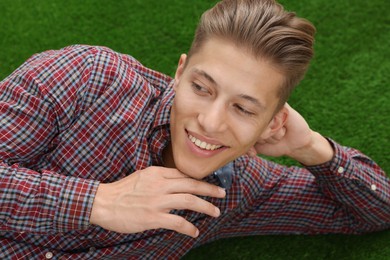Photo of Dream come true. Positive young man thinking about something while lying on green grass