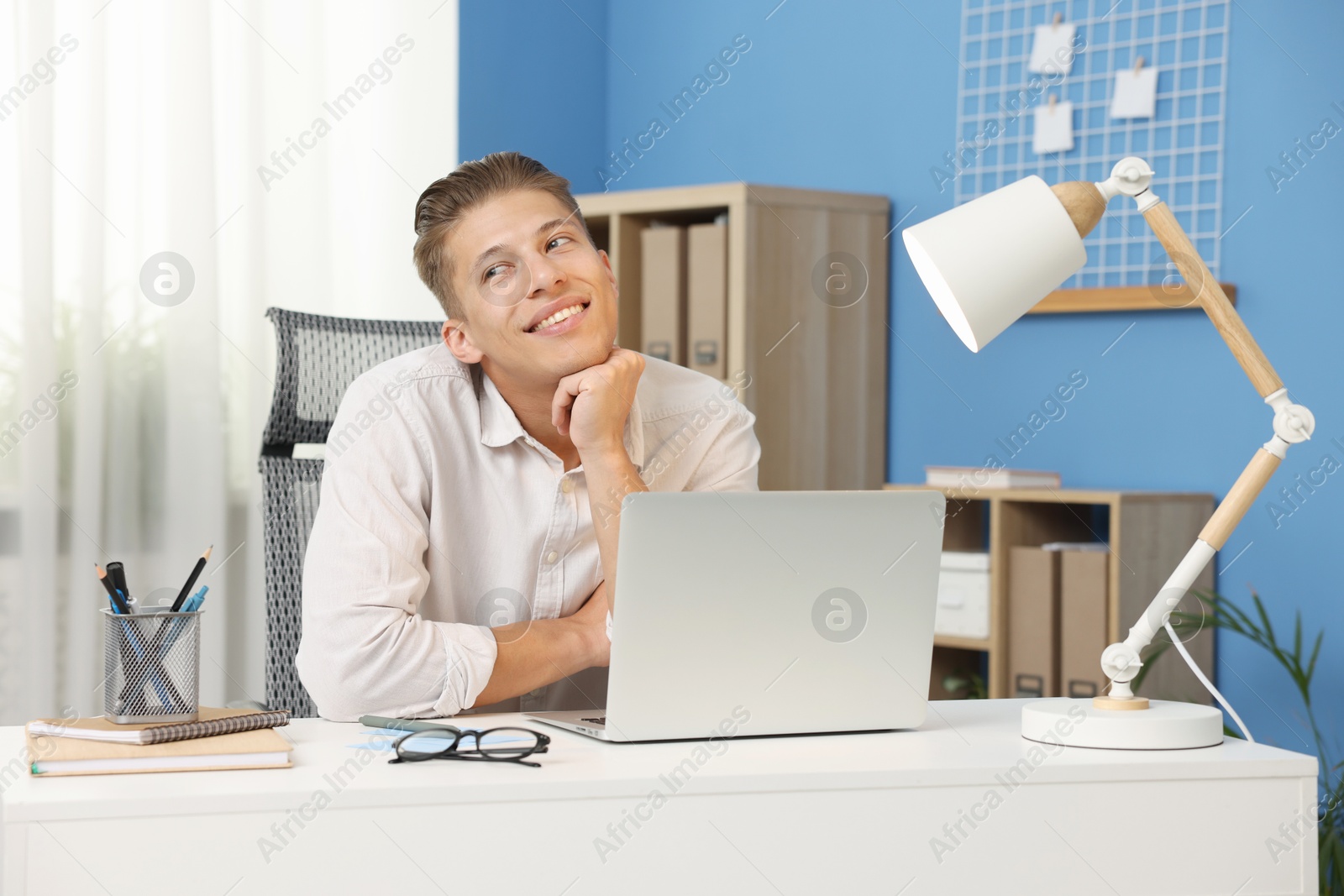 Dream come true. Positive young man thinking about something at desk indoors Photo of Dream come true. Positive young man thinking about something at desk indoors