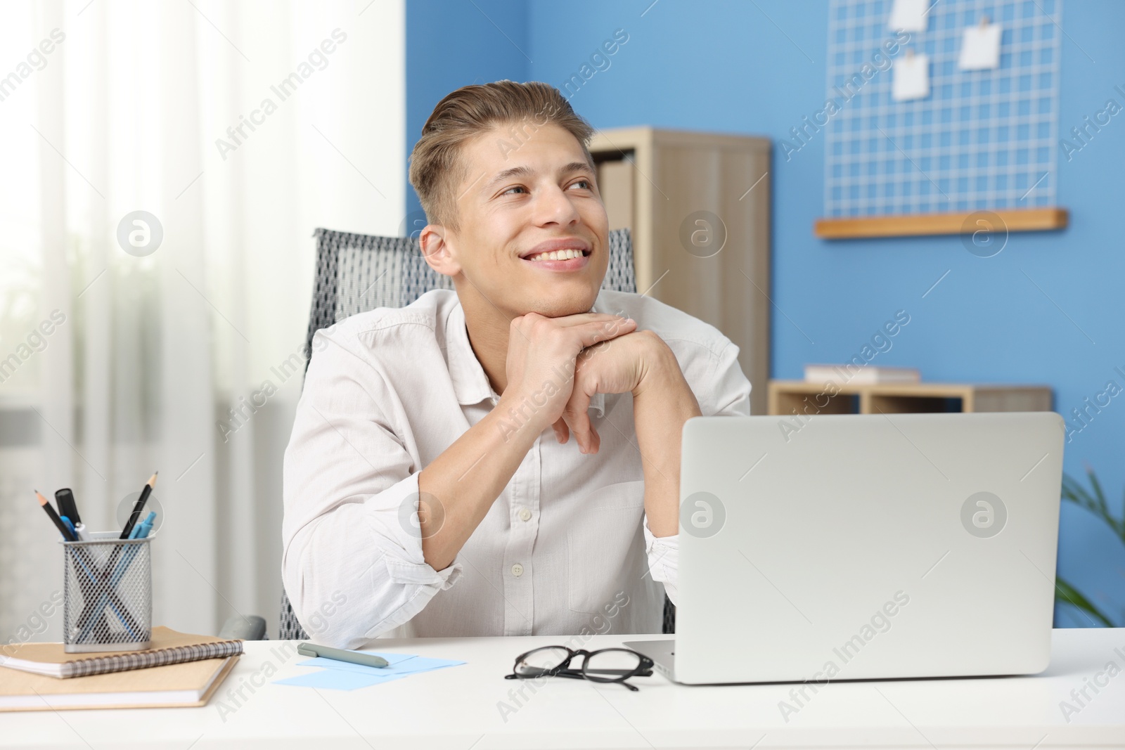 Dream come true. Positive young man thinking about something at desk indoors Photo of Dream come true. Positive young man thinking about something at desk indoors