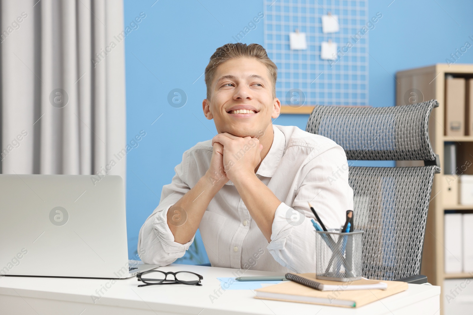 Dream come true. Positive young man thinking about something at desk indoors Photo of Dream come true. Positive young man thinking about something at desk indoors