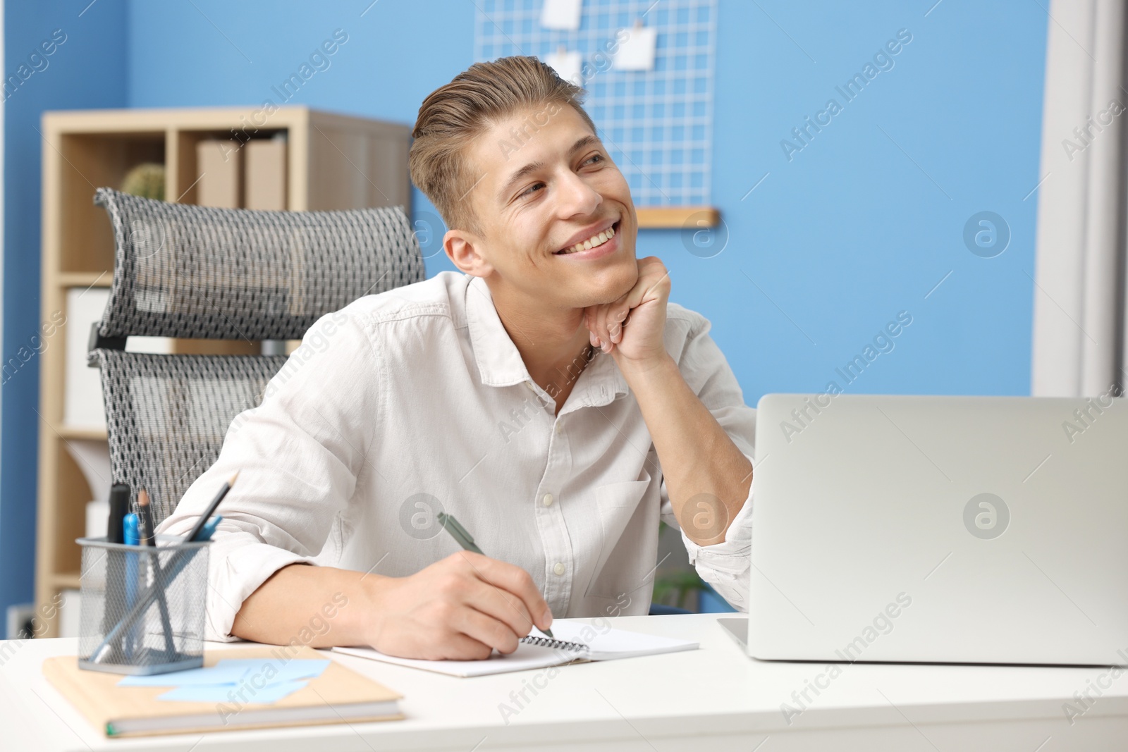 Dream come true. Positive young man thinking about something at desk indoors Photo of Dream come true. Positive young man thinking about something at desk indoors
