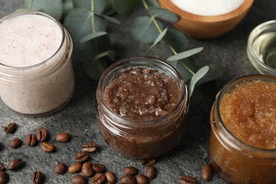 Photo of Natural body scrubs in glass jars and ingredients on grey table, closeup