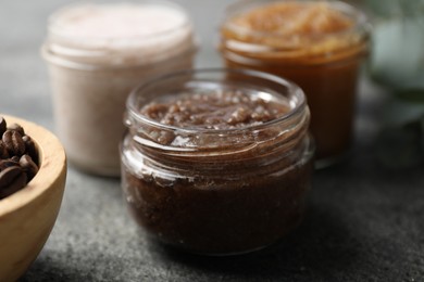 Photo of Natural body scrubs in glass jars and coffee beans on grey table, closeup