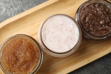 Photo of Natural body scrubs in glass jars on grey table, top view