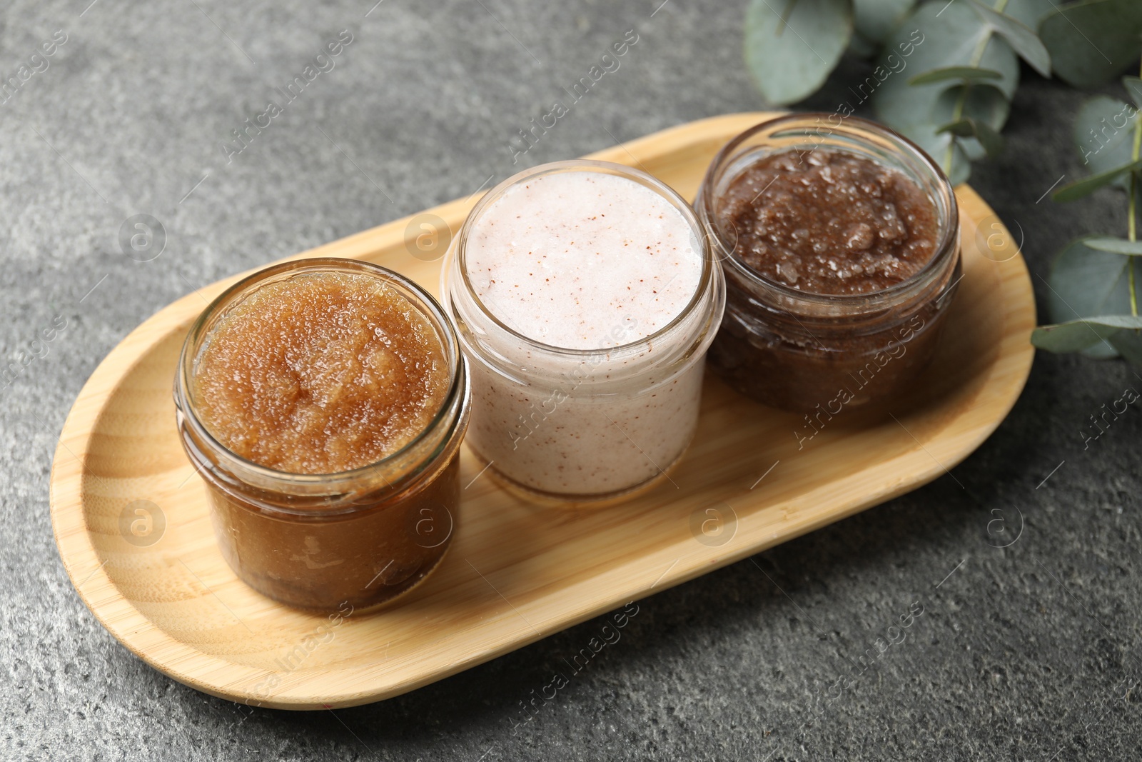 Natural body scrubs in glass jars and eucalyptus branches on grey table, closeup Photo of Natural body scrubs in glass jars and eucalyptus branches on grey table, closeup