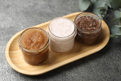 Photo of Natural body scrubs in glass jars and eucalyptus branches on grey table, closeup