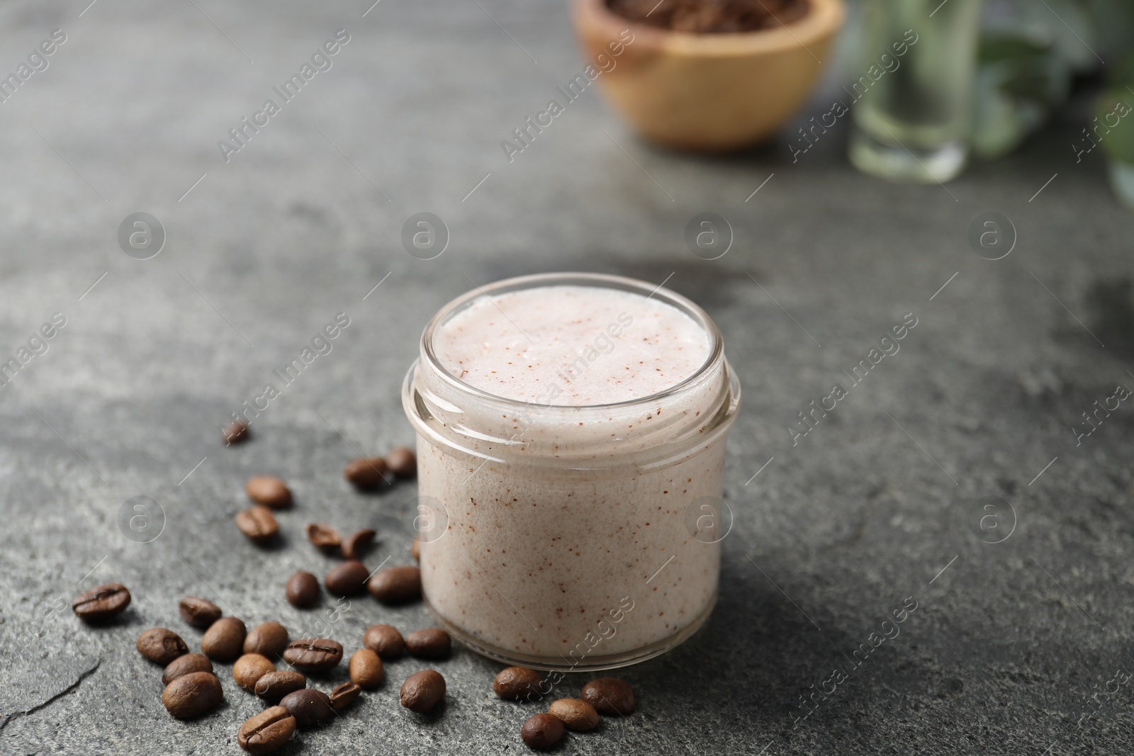Photo of Natural body scrub in glass jar and coffee beans on grey table, closeup