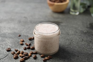 Photo of Natural body scrub in glass jar and coffee beans on grey table, closeup