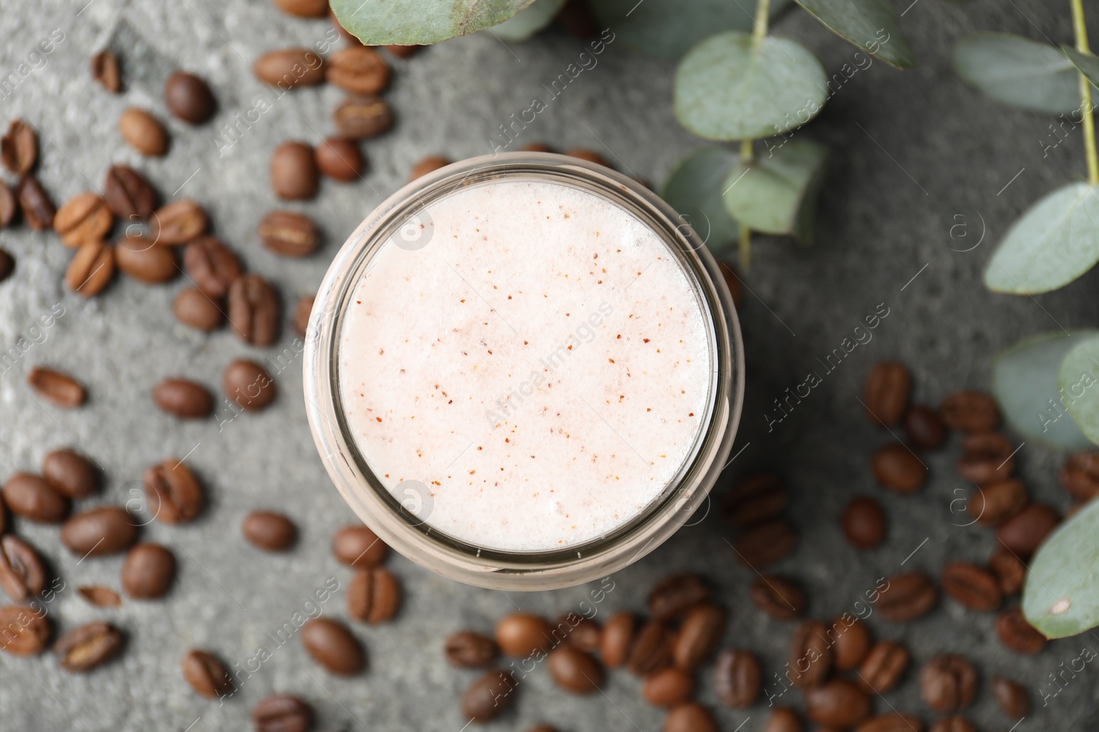 Photo of Natural body scrub in glass jar, coffee beans and eucalyptus branches, flat lay