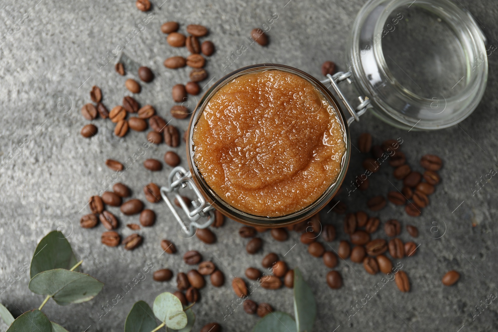 Photo of Natural body scrub in glass jar, coffee beans and eucalyptus branches, flat lay