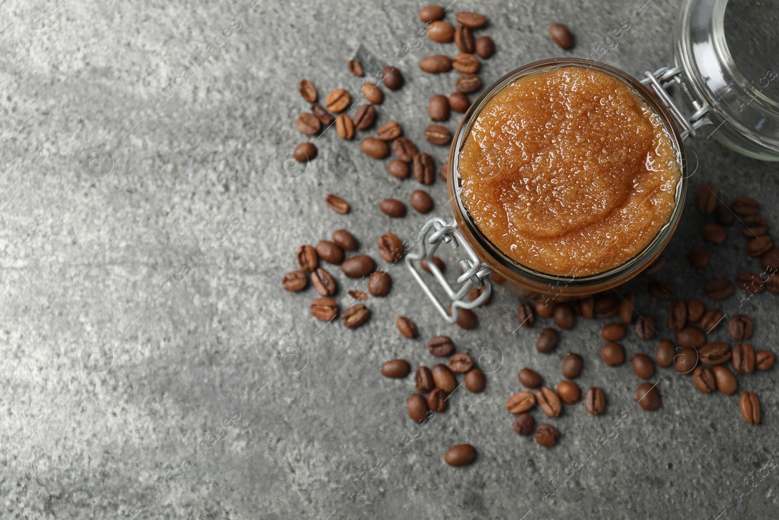 Photo of Natural body scrub in glass jar and coffee beans on grey table, flat lay. Space for text