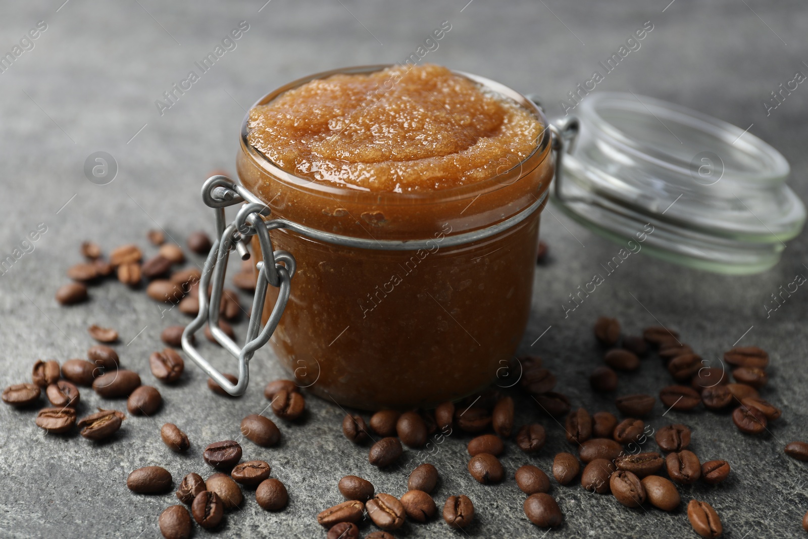 Photo of Natural body scrub in glass jar and coffee beans on grey table, closeup