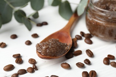 Photo of Natural body scrub, coffee beans and eucalyptus branches on white wooden table, closeup