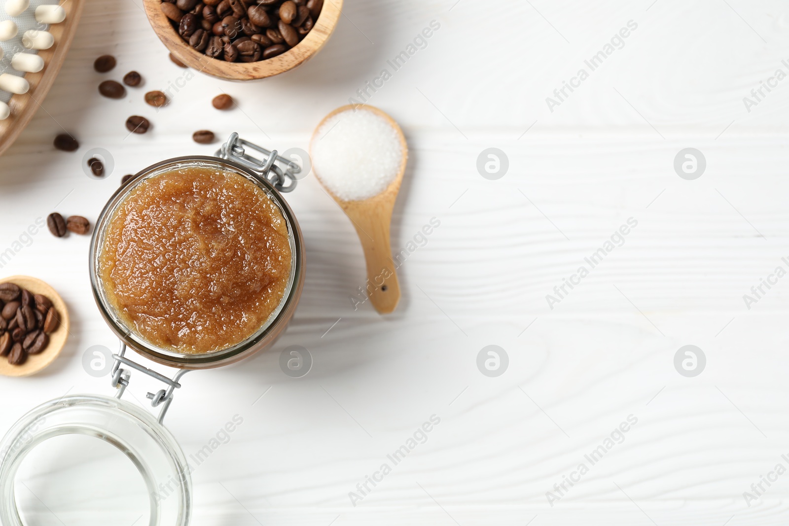 Photo of Natural body scrub in glass jar, ingredients and brush on white wooden table, flat lay. Space for text