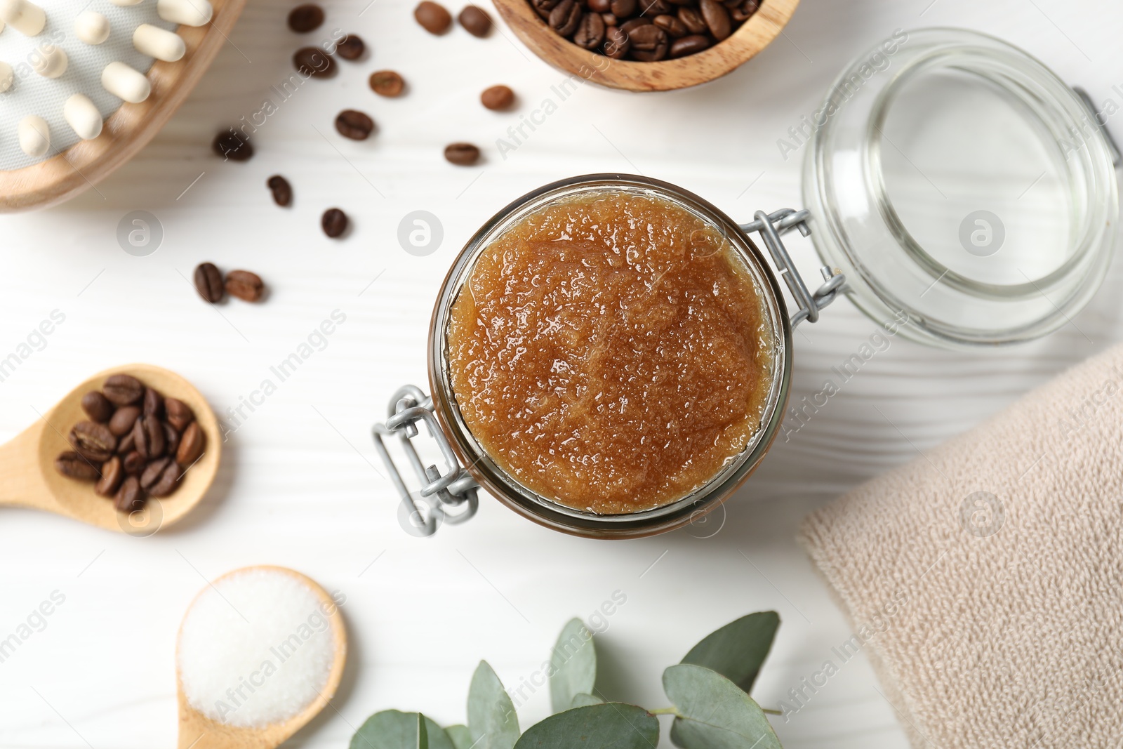 Photo of Natural body scrub in glass jar, ingredients and brush on white wooden table, flat lay
