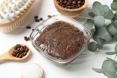 Photo of Natural body scrub in glass bowl, ingredients and brush on white wooden table, closeup