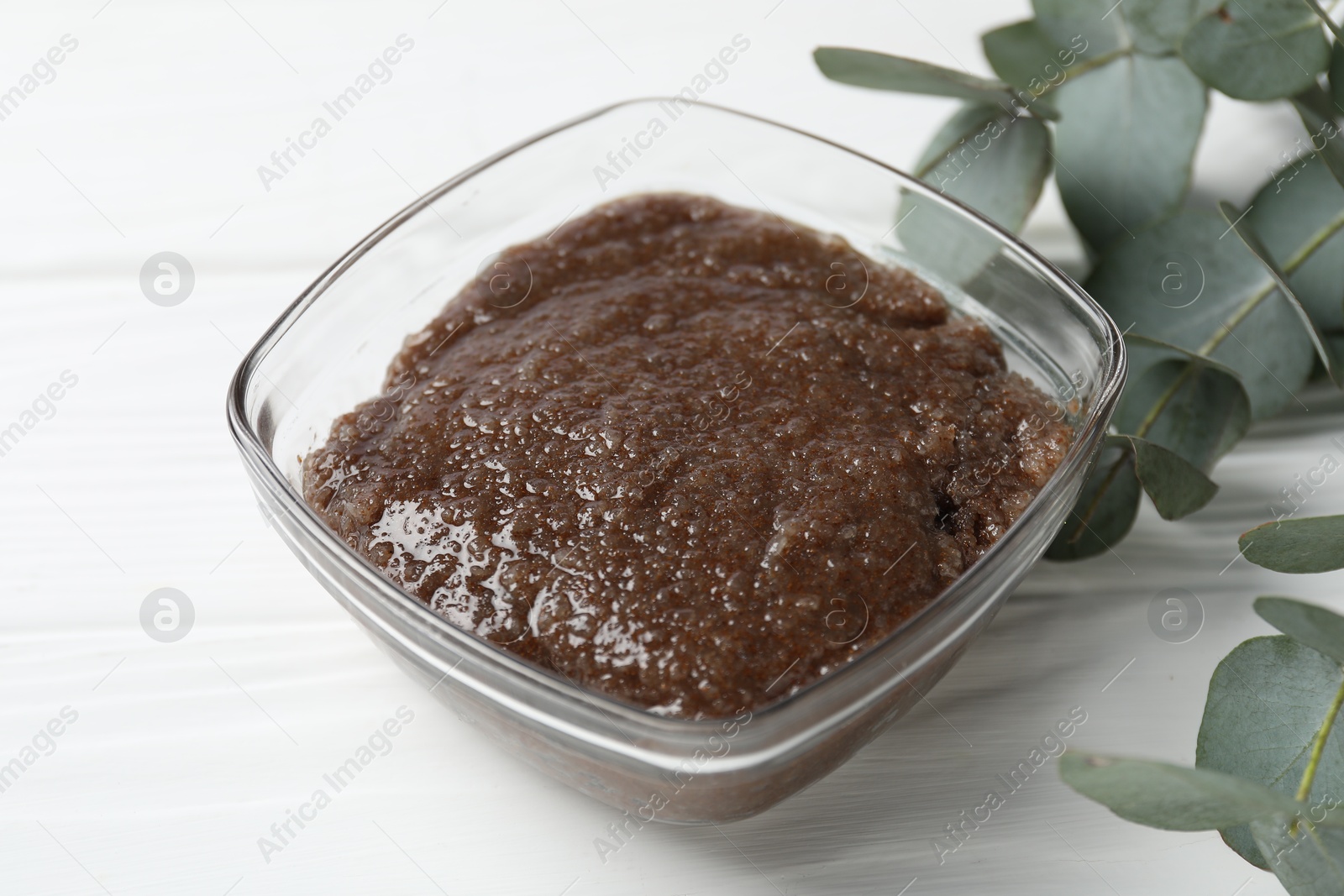 Natural body scrub in glass bowl and eucalyptus branches on white wooden table, closeup Photo of Natural body scrub in glass bowl and eucalyptus branches on white wooden table, closeup