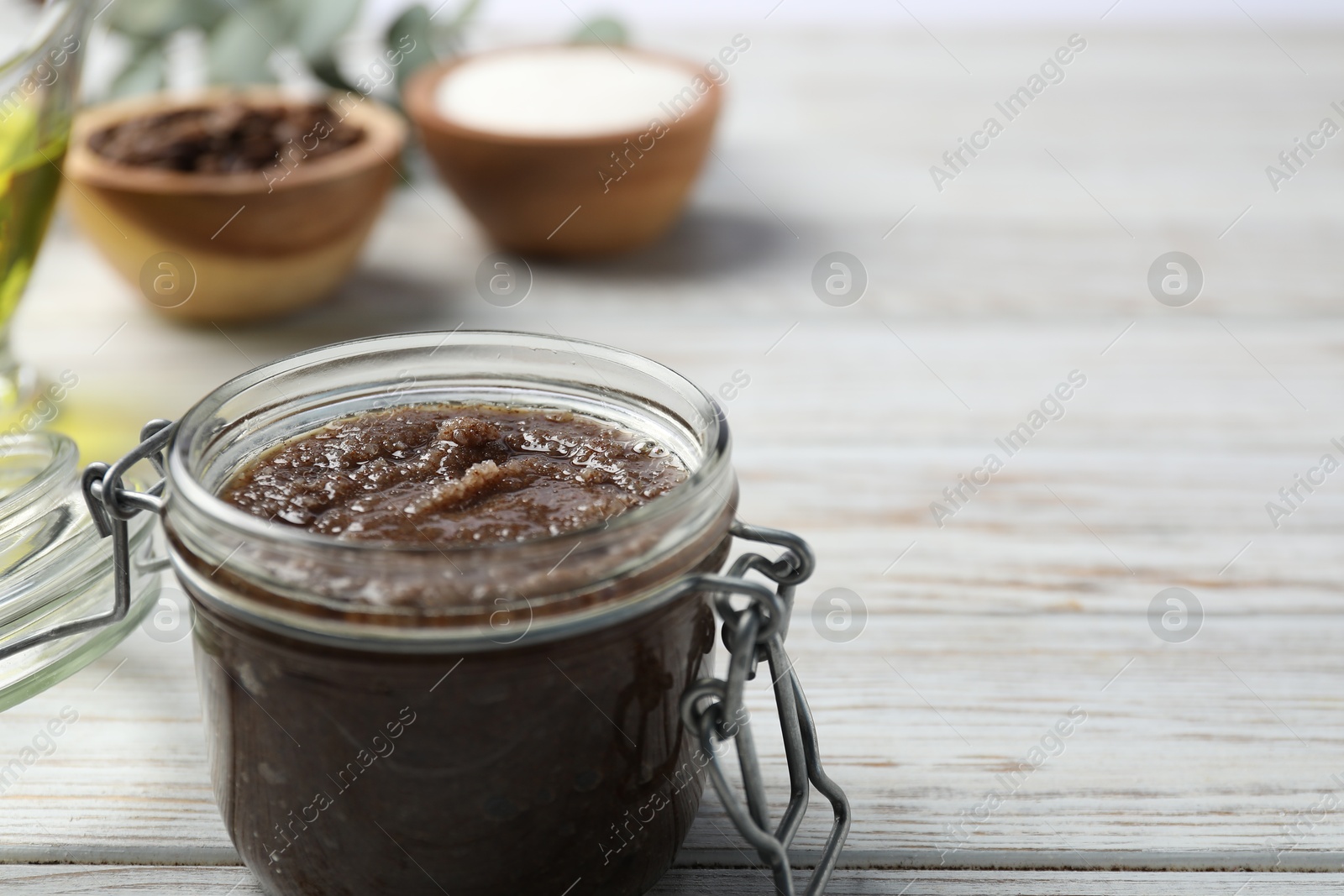 Photo of Natural body scrub in glass jar and ingredients on wooden table, closeup. Space for text