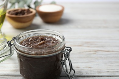 Photo of Natural body scrub in glass jar and ingredients on wooden table, closeup. Space for text