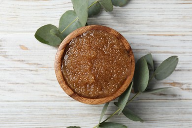 Photo of Natural body scrub in bowl and eucalyptus branches on wooden table, flat lay